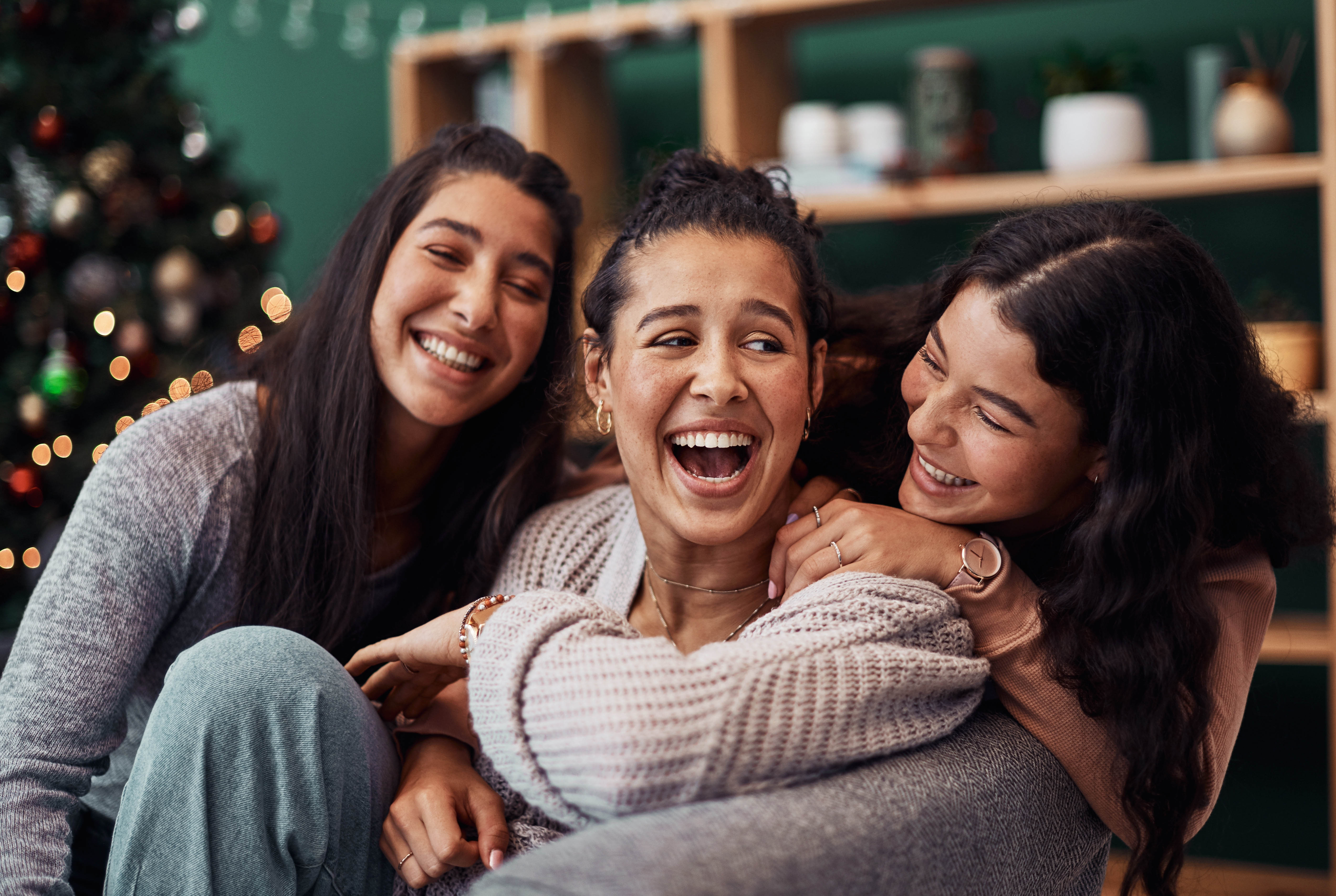 Three women sitting on the couch in front of the Christmas tree, laughing together